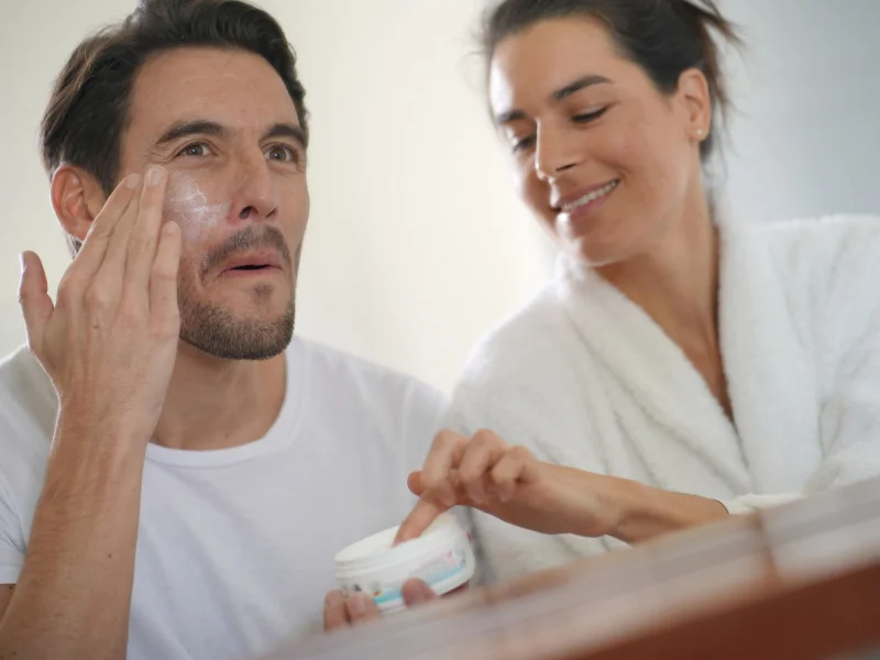 um casal de um homem e uma mulher a aplicar um creme de rosto com niacinamida