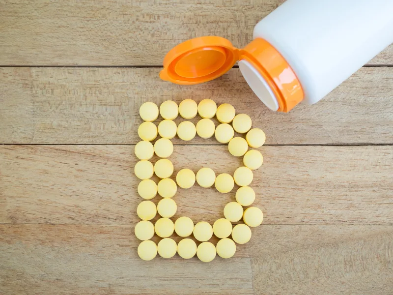 Um frasco de suplemento de vitamina B3 deitado numa mesa e os comprimidos a formar a letra B
