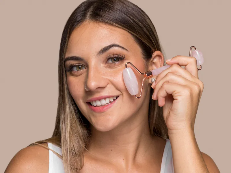 uma mulher sorridente a aplicar creme de contorno de olhos com acessório metálico