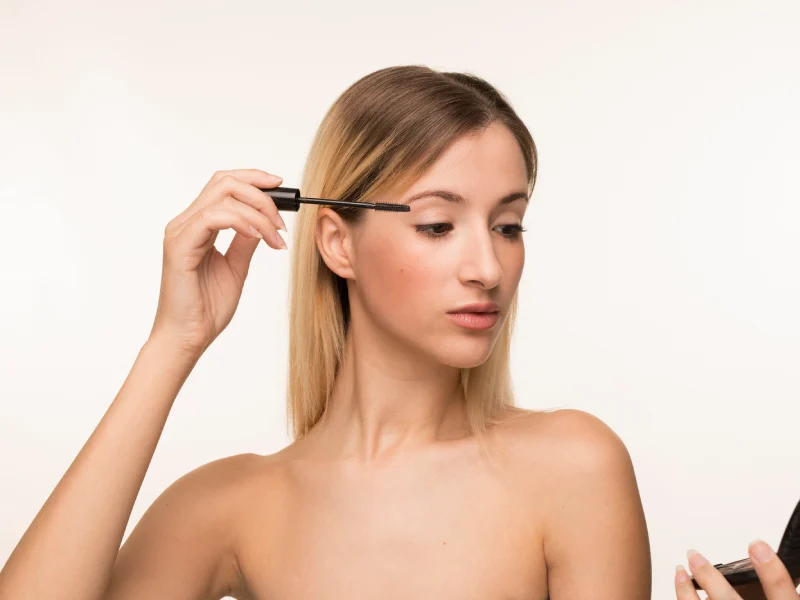 mulher a aplicar rimel com pequeno espelho na mão