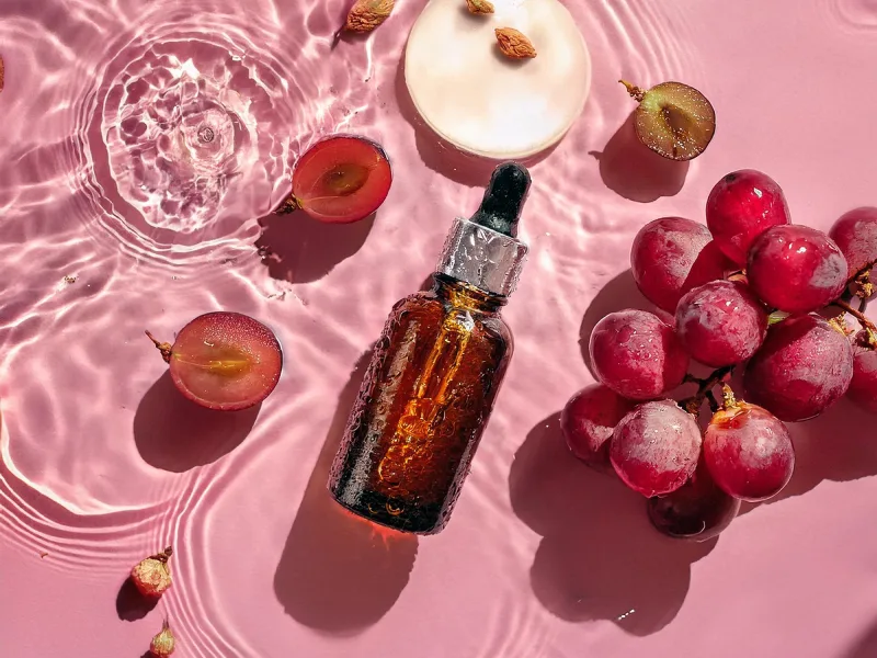 sérum de resveratrol pousado ao lado de uvas e frutos secos num fundo com água cor de rosa