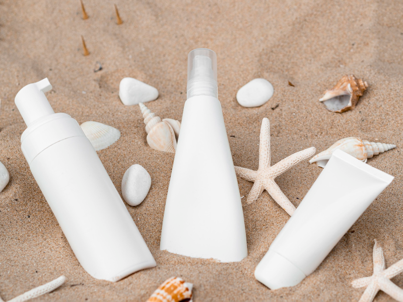 3 embalagens de protetor solar na areia rodeados de conchas